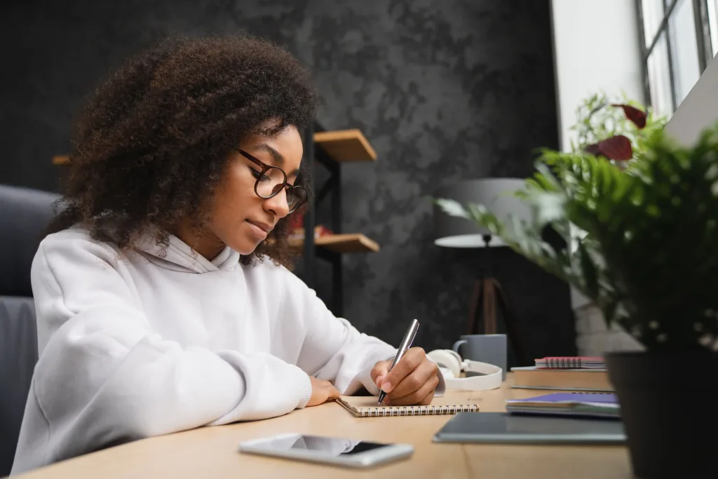 Student doing homework, writing in copybook using smartphone. E-learning. Homeschool.